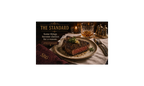 Steak on a plate with a glass of whiskey, accompanied by 'The Standard' branding.