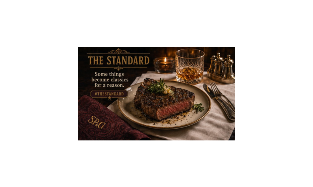 Steak on a plate with a glass of whiskey, accompanied by 'The Standard' branding.